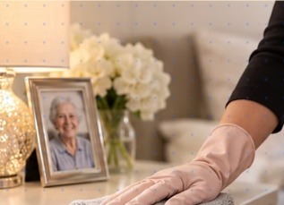 A cleaner hand-polishing a sideboard beside fresh flowers and a framed photo